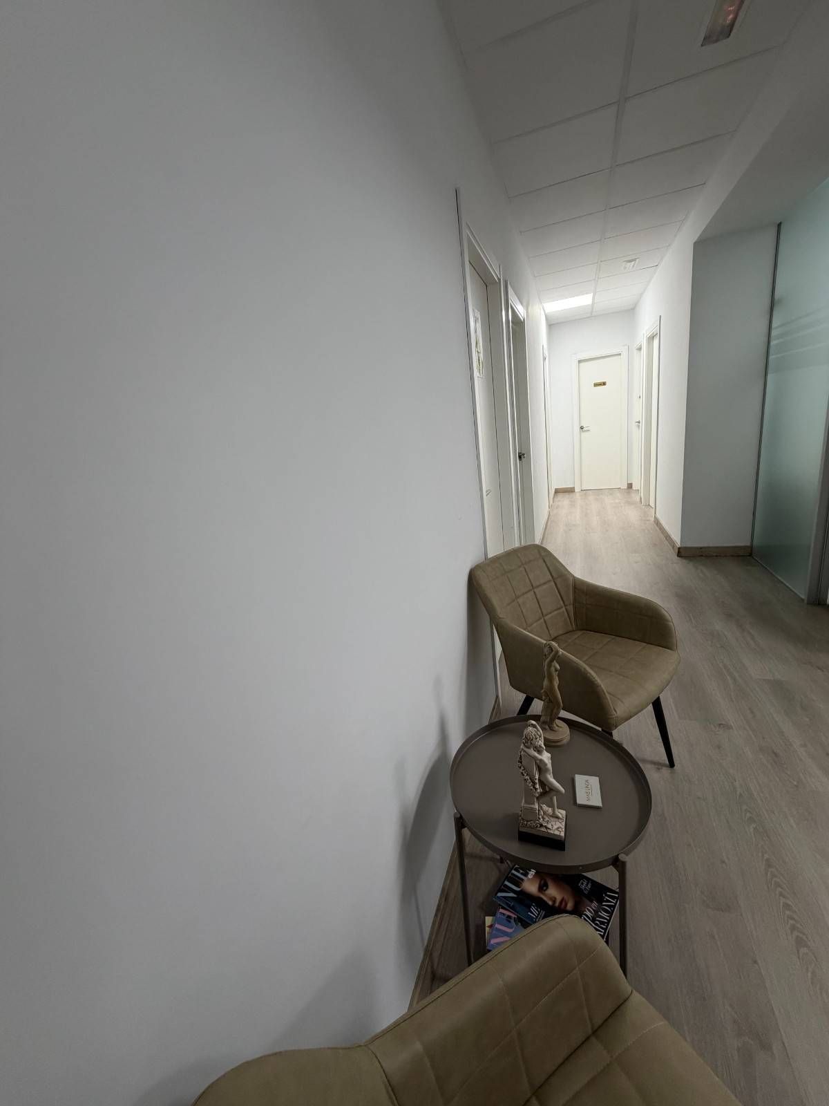 Un pasillo de espera en tonos neutros con dos sillones modernos y una pequeña mesa auxiliar.