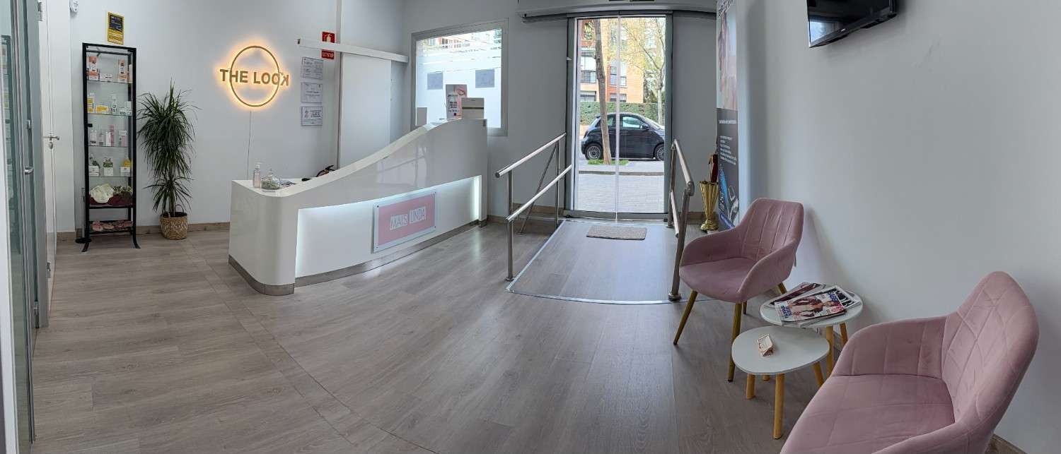 Vestíbulo luminoso y moderno con mostrador de recepción blanco, dos sillones rosas.