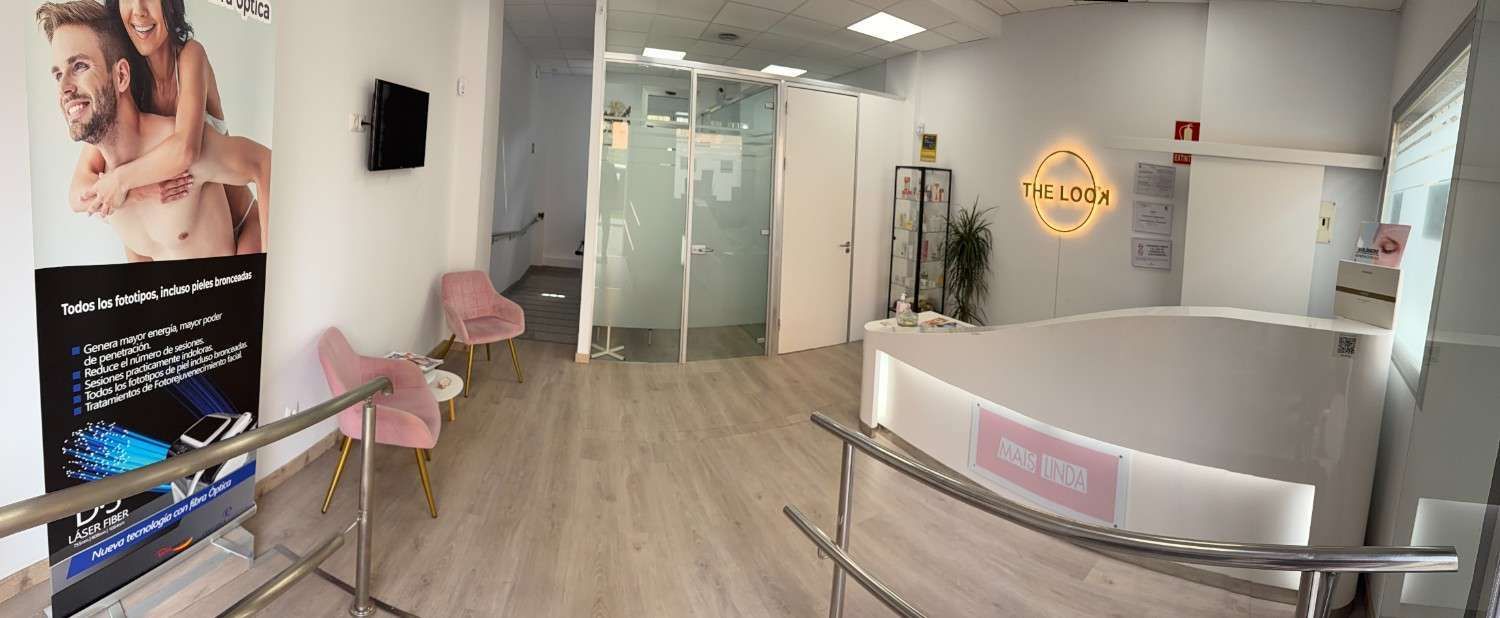 Una luminosa sala de espera con suelo de madera clara, sillas rosas, un mostrador de recepción .