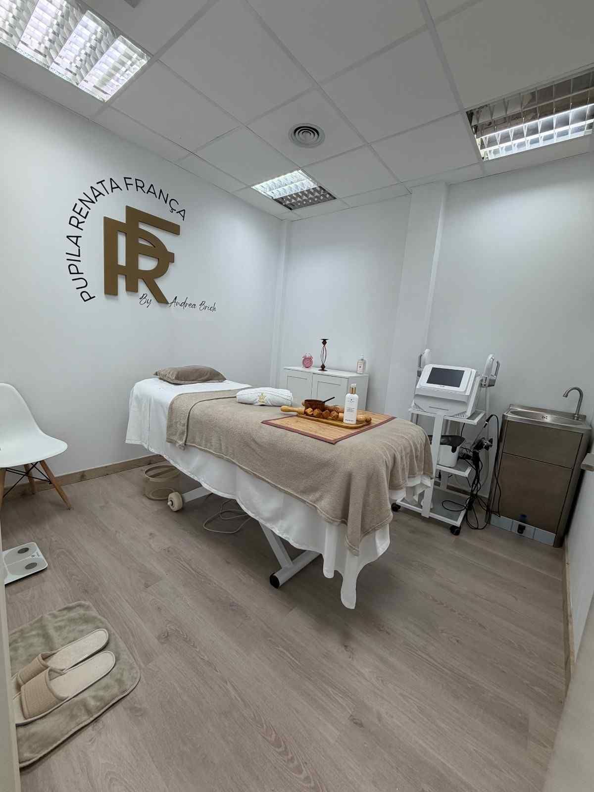 Una sala de tratamientos de spa con una camilla de masaje, muebles blancos, un logotipo en la pared.