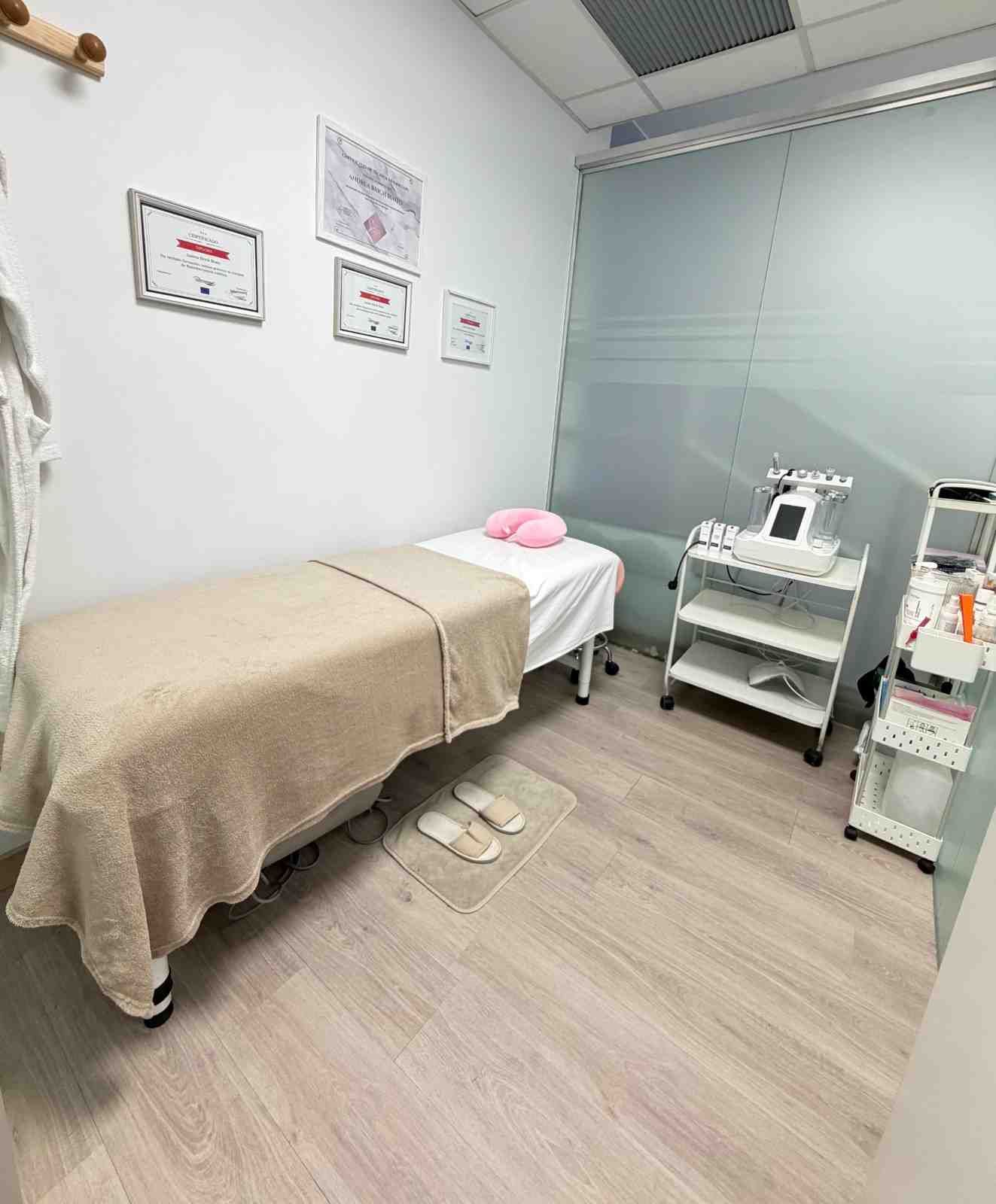 Una sala de tratamientos de spa con una camilla de masaje, un pequeño carrito con ruedas, equipo médico.