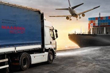 Ein LKW fährt auf einer Straße neben einem Schiff her, über ihm fliegt ein Flugzeug.