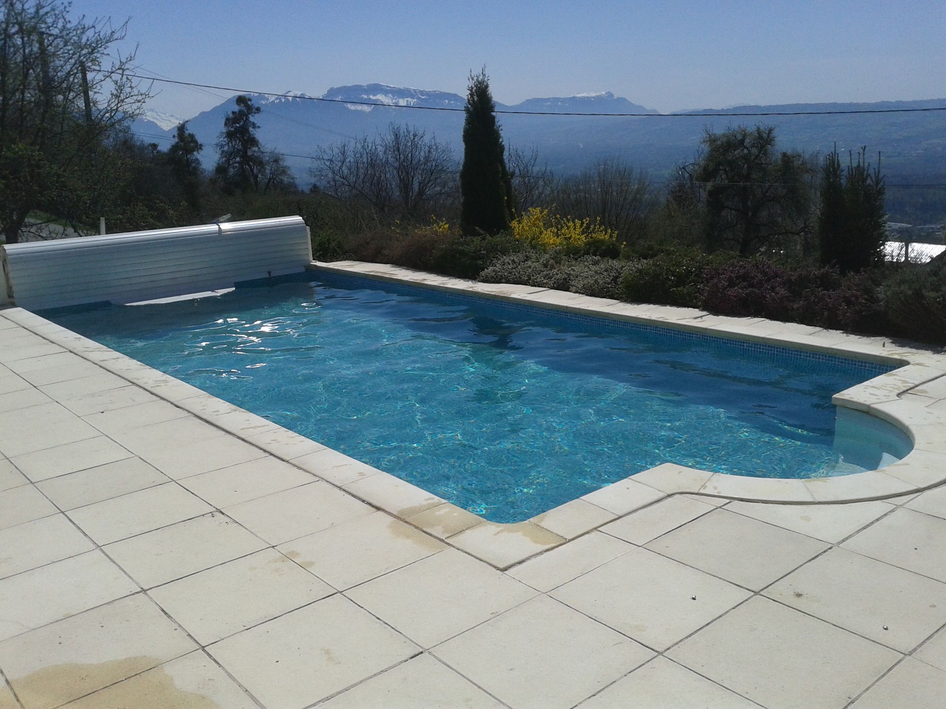 Piscine extérieure bordée d’une terrasse carrelée, avec une vue sur les montagnes.