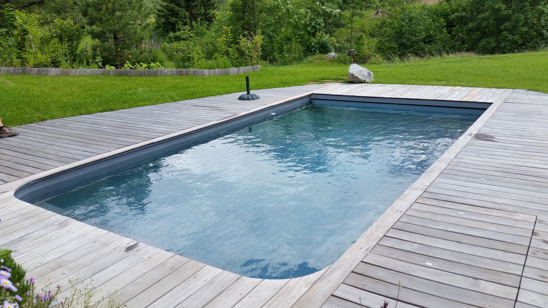 Piscine rectangulaire dans un jardin entouré d’une terrasse et d’une pelouse.
