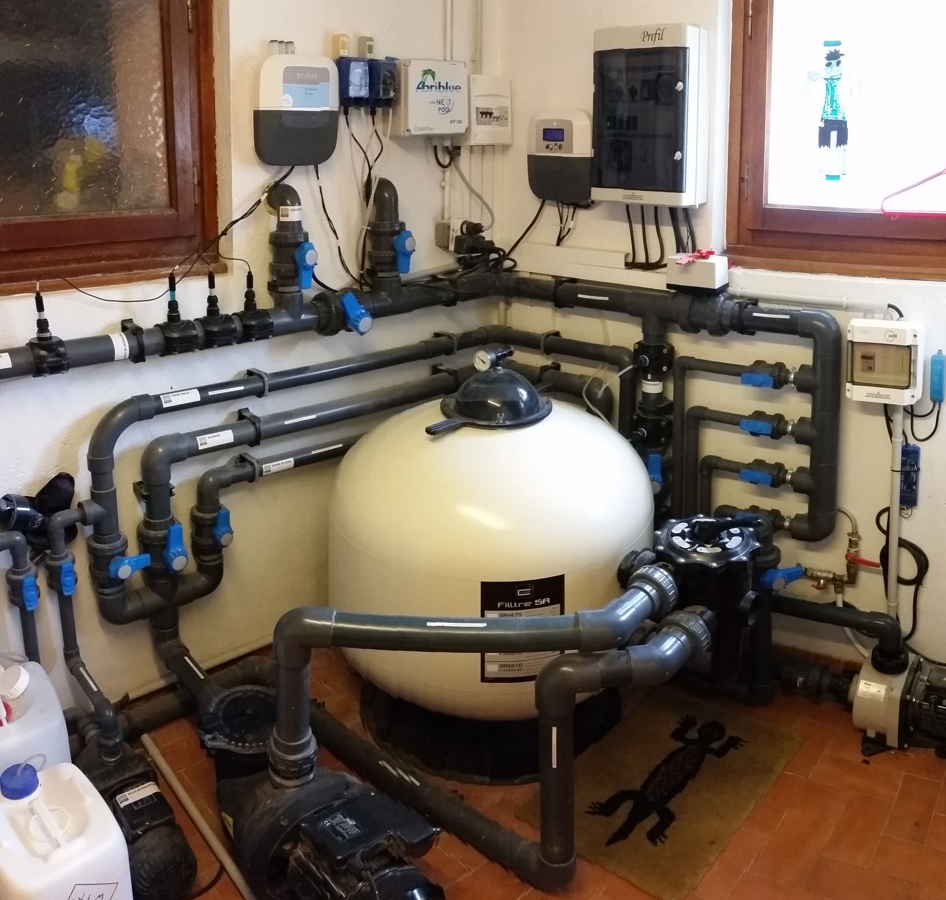 Local technique de filtration de piscine intérieure avec cuve, tuyaux, vannes et équipements de commande muraux.