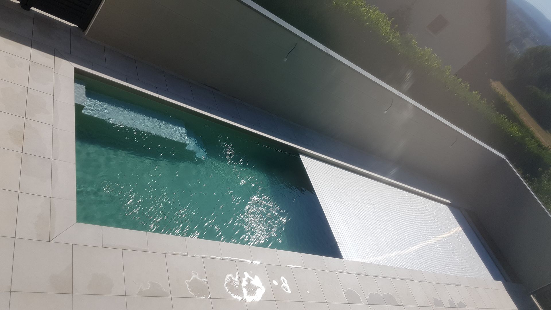 Piscine rectangulaire moderne bordée d’une terrasse carrelée, avec une chaise longue blanche.
