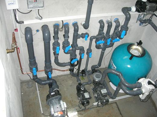 Équipement de filtration avec des tuyaux, des vannes et un réservoir de pression dans un local technique.