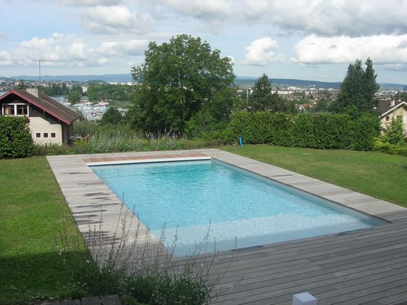 Piscine dans le jardin entouré de pelouse et de haies, surplombant une ville au loin.