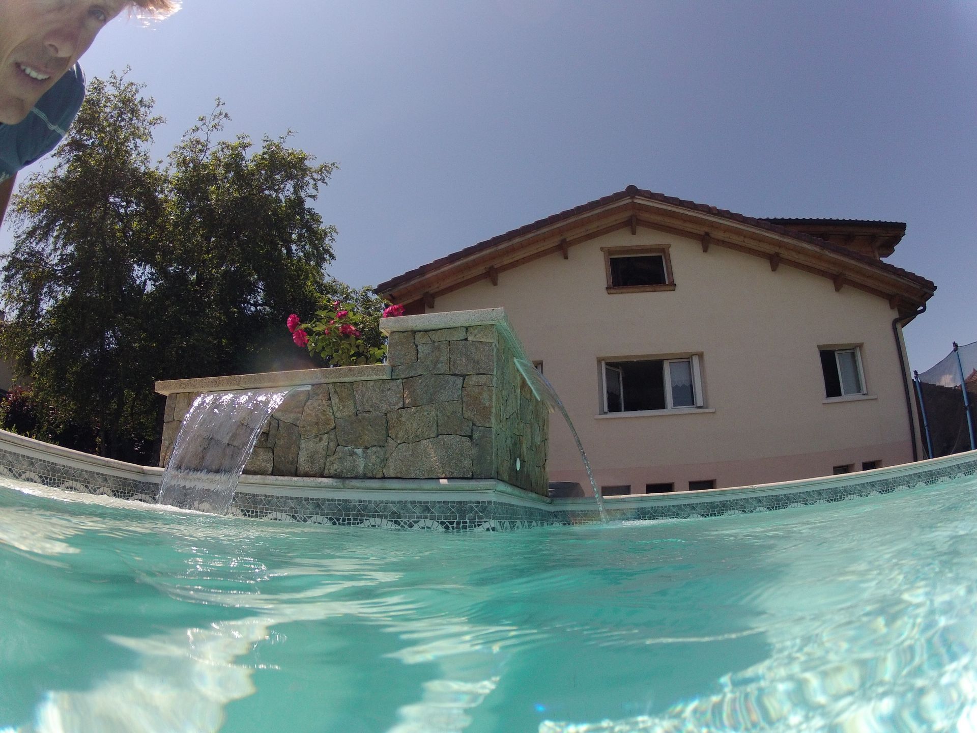 Vue d’une maison depuis une piscine à demi immergée, avec une petite cascade.