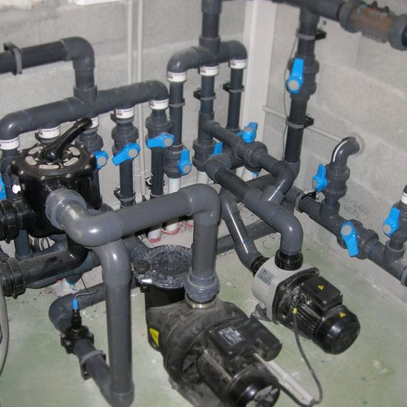 Collecteur de plomberie avec des tuyaux en PVC et des vannes dans un local technique.