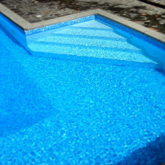 Une piscine avec des marches et une margelle en pierre.