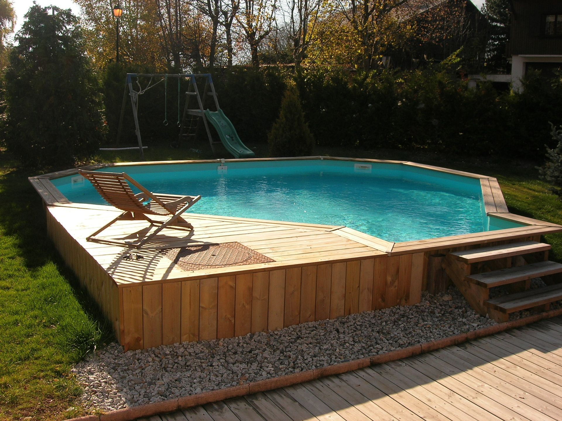 Piscine hors-sol dans le jardin, avec terrasse en bois, chaises longues et marches.