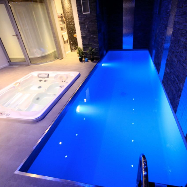 Piscine intérieure éclairée en bleu, à côté d’un bain à remous et d’un mur de briques.