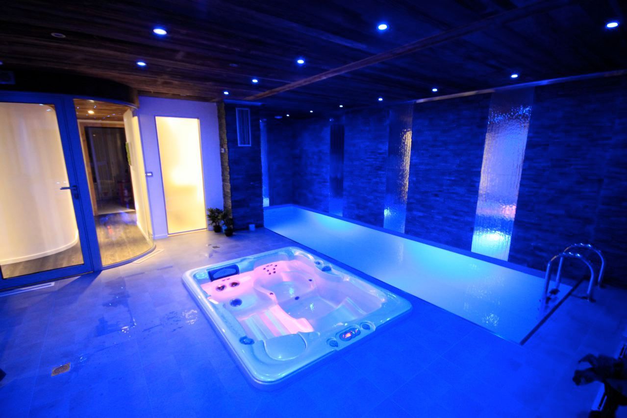 Salle de spa intérieure baignée de lumière bleue, avec un jacuzzi et un espace piscine carrelé.