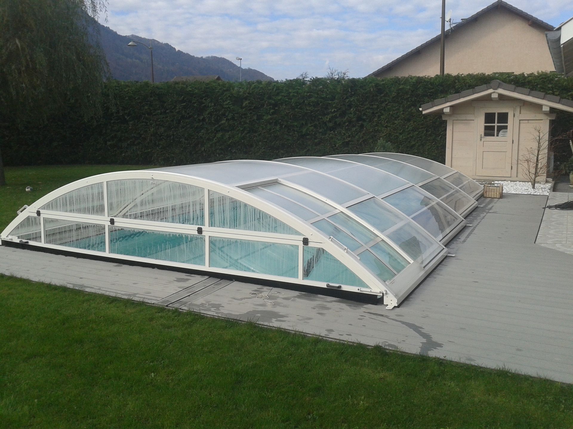 Piscine couverte dans un jardin, avec un abri à côté d’une pelouse et d’une maison.