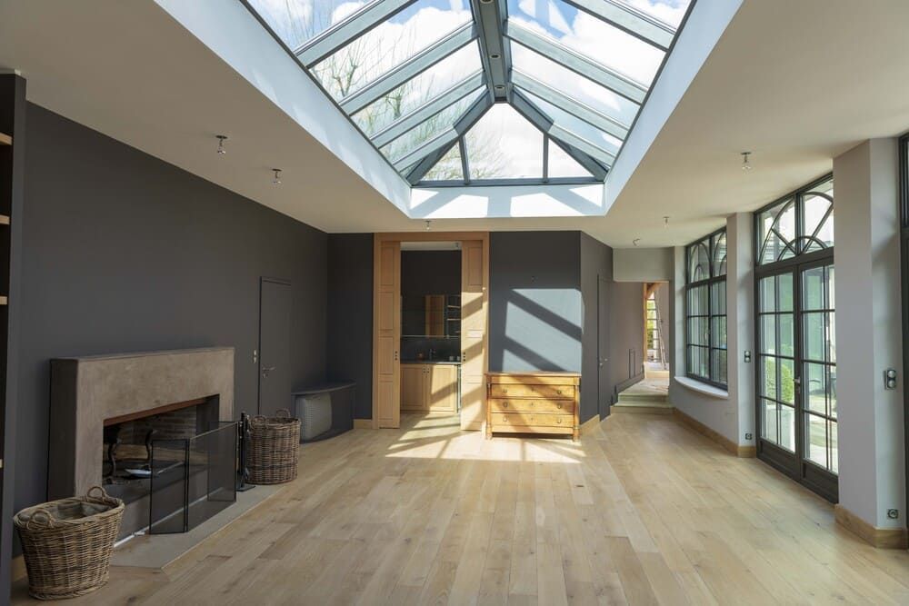 Pièce spacieuse et moderne avec des murs gris foncé, un parquet clair, une cheminée et un grand plafond vitré.