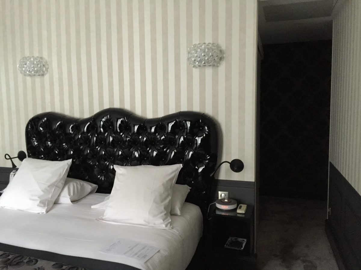Un lit avec une grande tête de lit noire capitonnée se détachant sur un papier peint à rayures dans une chambre faiblement éclairée.