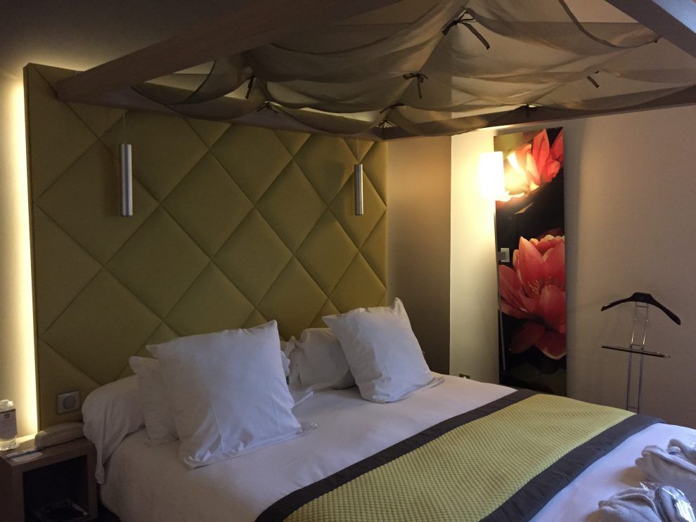 Un lit d'hôtel moderne avec une tête de lit capitonnée vert citron, des oreillers blancs, un chemin de lit jaune et un tissu décoratif à baldaquin au-dessus.