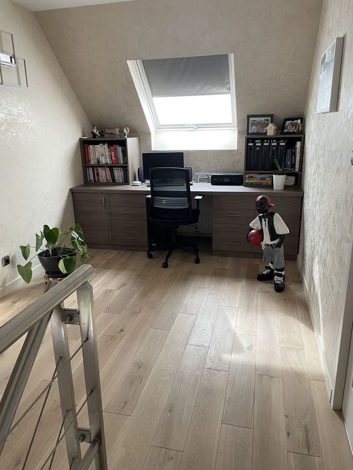 Un bureau à domicile aménagé dans un grenier, avec un parquet clair, un bureau gris intégré, une chaise de bureau noire et une figurine de basket-ball.