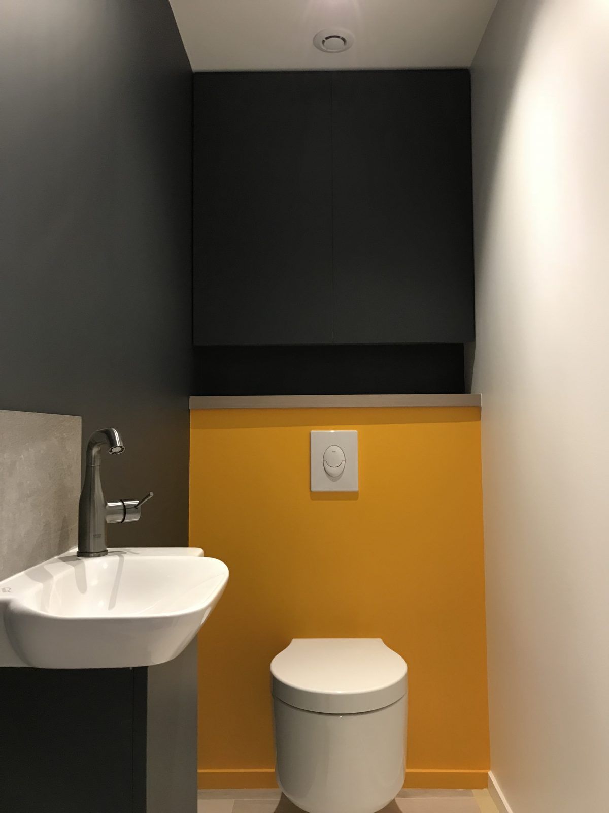 Des toilettes modernes avec des WC et un lavabo blancs contre un mur anthracite et un mur d'accent jaune vif.