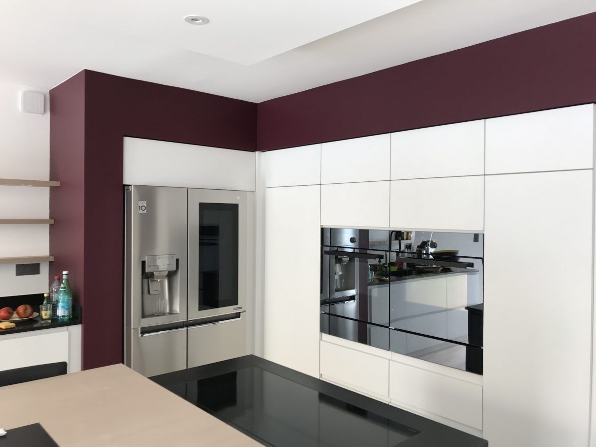Une cuisine moderne avec des armoires blanches, un réfrigérateur en acier inoxydable, un four encastré et un mur d'accent bordeaux foncé.