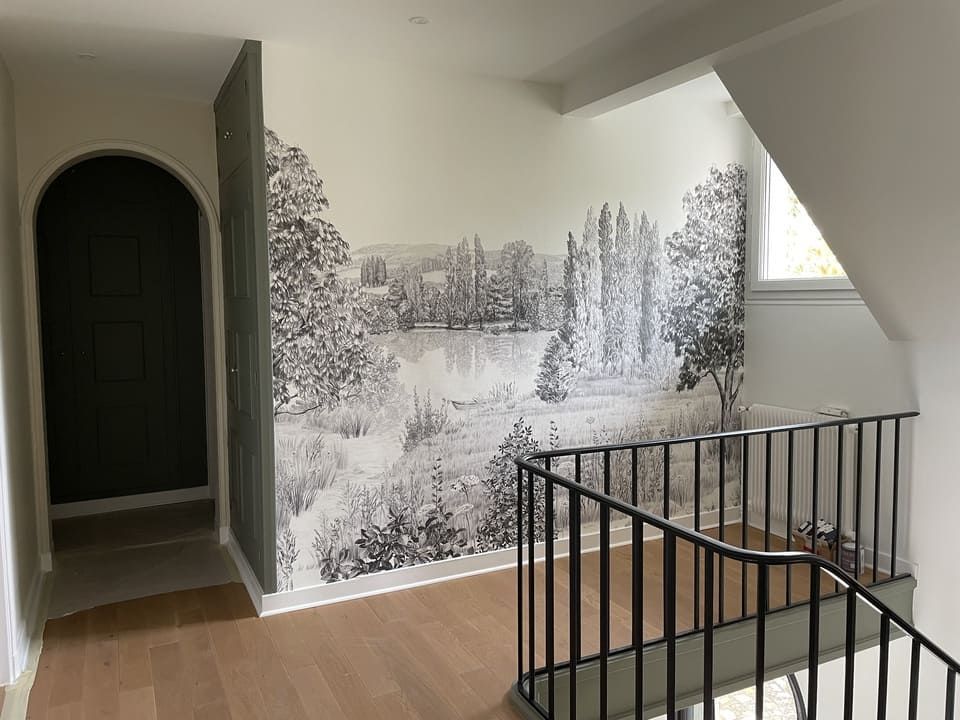Un palier avec parquet et rampe noire, orné d'une grande fresque murale monochrome représentant un paysage.