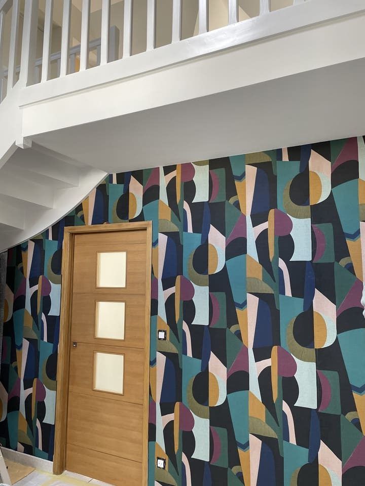 Une porte en bois moderne encastrée dans un mur recouvert d'un papier peint géométrique abstrait aux motifs audacieux, dans des tons de bleu marine, de turquoise et d'or.