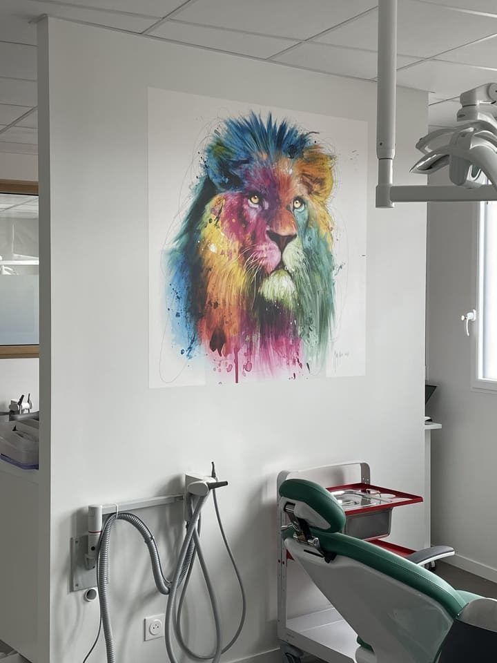Une aquarelle colorée représentant un lion est accrochée à un mur blanc dans une salle d'examen dentaire, à côté d'un fauteuil médical.