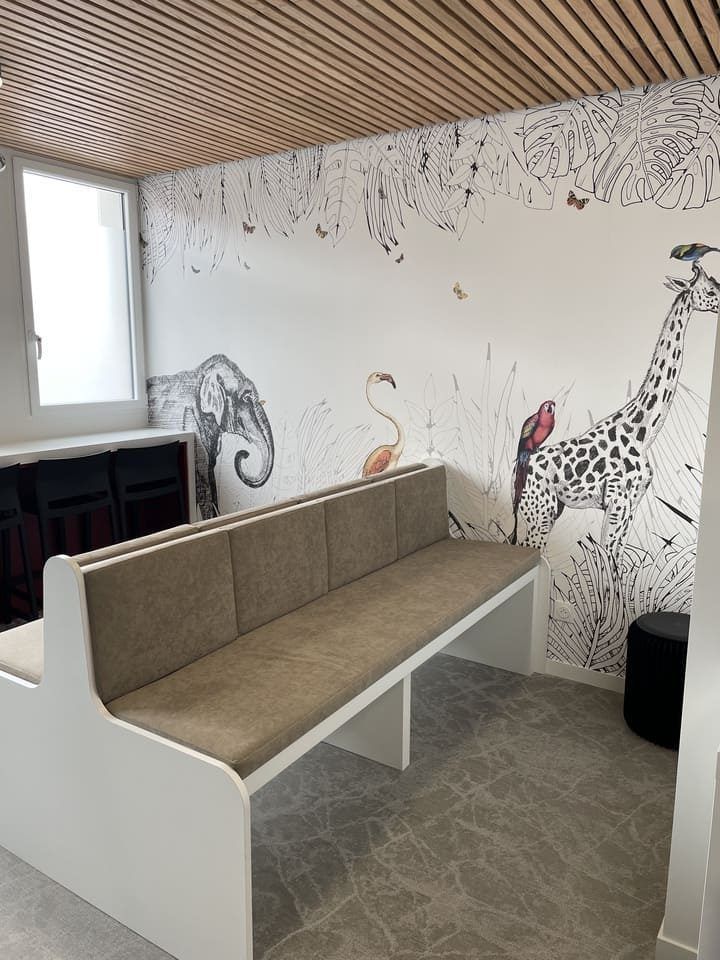 Une salle d'attente avec un banc beige et un papier peint à motifs animaliers représentant une girafe, un éléphant et un flamant rose.