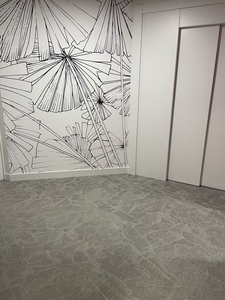 Un coin de pièce avec un sol gris à motifs et un mur blanc orné d'une fresque murale botanique en noir et blanc.