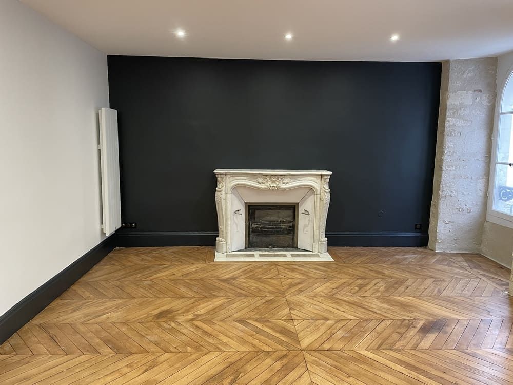 Une pièce avec un parquet en chevrons, un mur d'accent foncé et une cheminée décorative en pierre blanche.