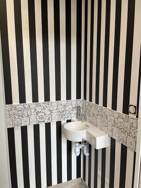 Un petit lavabo mural dans un coin, adossé à des murs à rayures verticales noires et blanches et à une crédence à motifs.