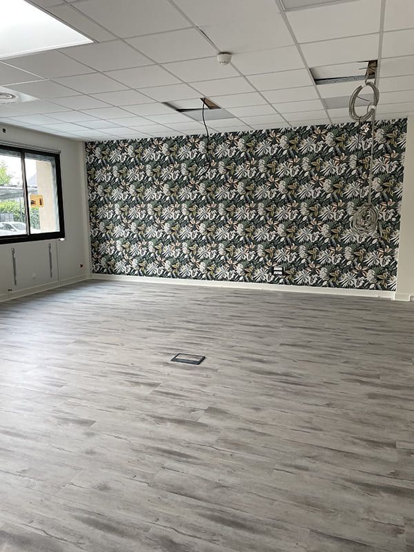 Une pièce dotée d'un parquet clair imitation bois, de murs blancs, d'un mur d'accent floral foncé et d'un plafond suspendu.