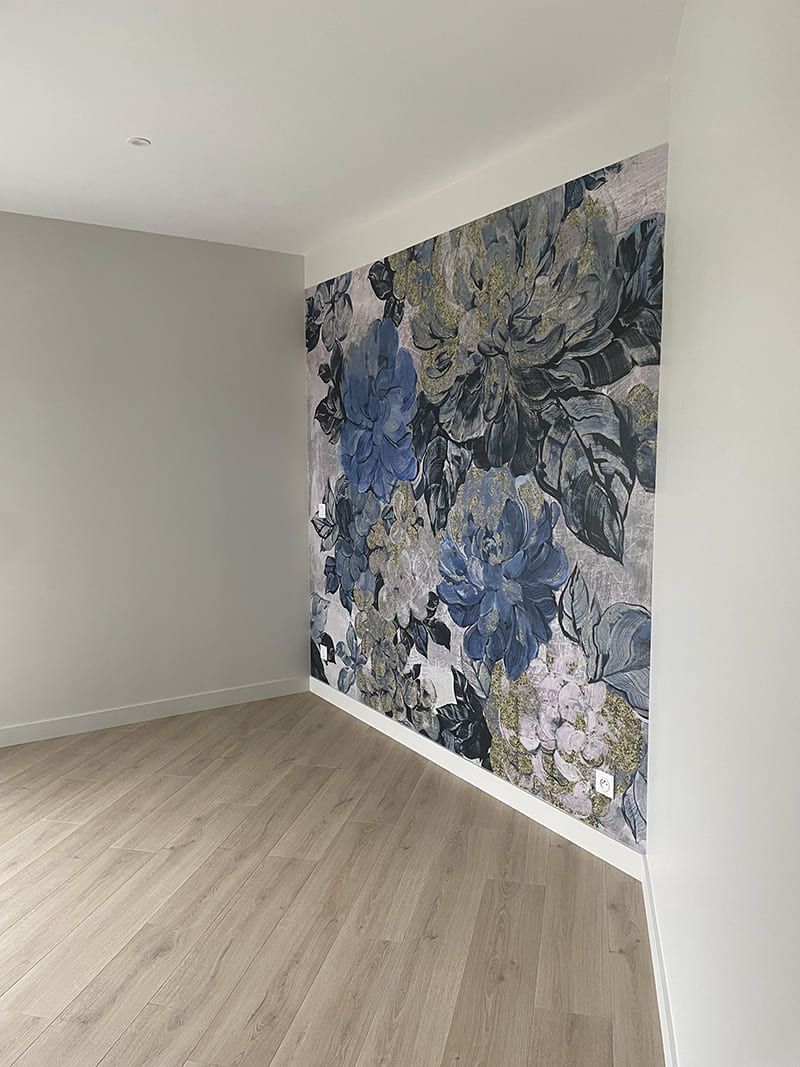Un coin de pièce avec parquet clair et murs blancs unis, agrémenté d'un mur d'accent recouvert d'un papier peint à grands motifs floraux bleus.