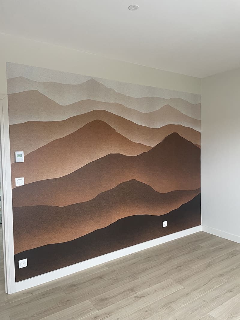 Une fresque murale représentant des chaînes de montagnes abstraites et superposées dans différentes nuances de brun et de beige, à l'intérieur d'une pièce.