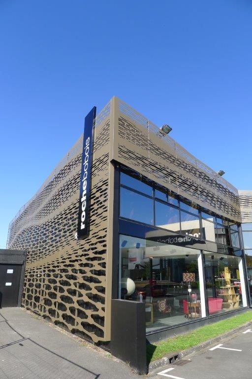 Un showroom de meubles Roche Bobois avec un mur extérieur distinctif en métal beige découpé au laser, sous un ciel bleu clair.