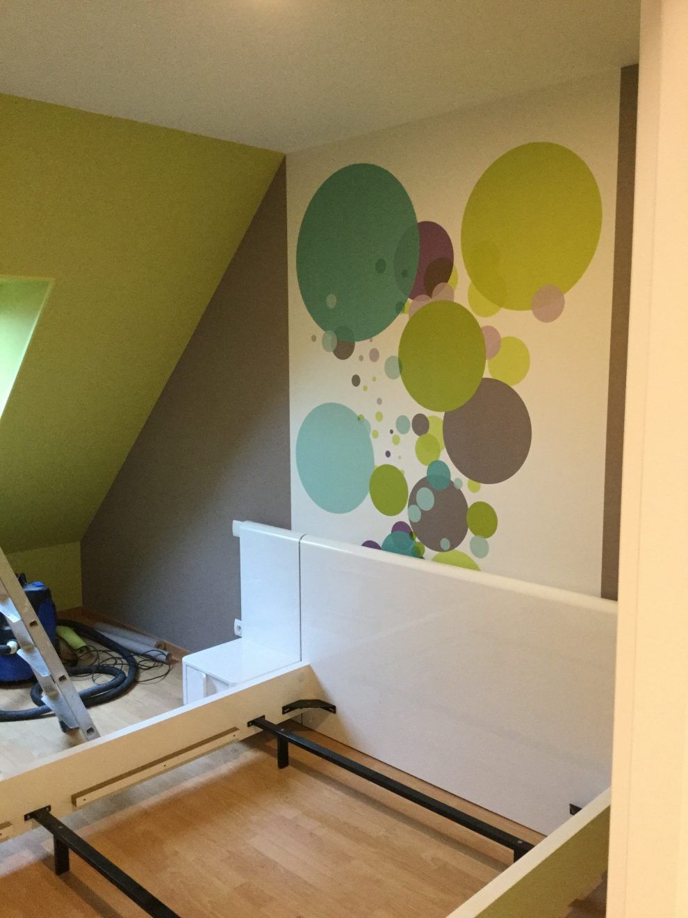 Une chambre avec un mur en pente peint en vert et marron, et un mur d'accent orné d'une fresque de cercles colorés de différentes tailles.