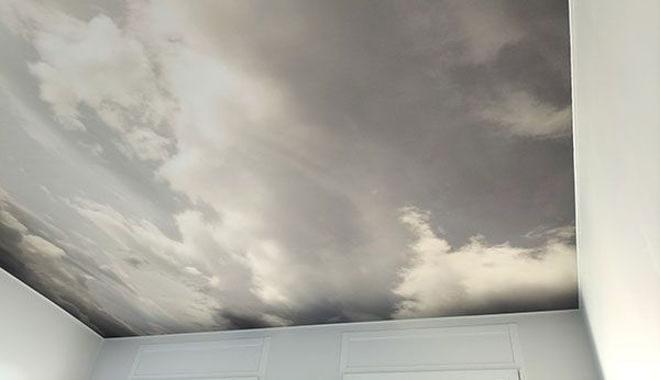 Une fresque au plafond représentant un ciel nuageux réaliste et dramatique dans des tons de gris et de blanc.