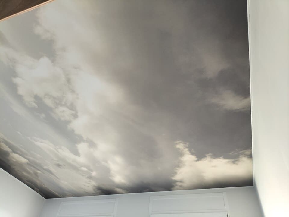 Un plafond orné d'une fresque réaliste représentant un ciel nuageux et couvert, dans des tons de gris, de blanc et de bleu clair.
