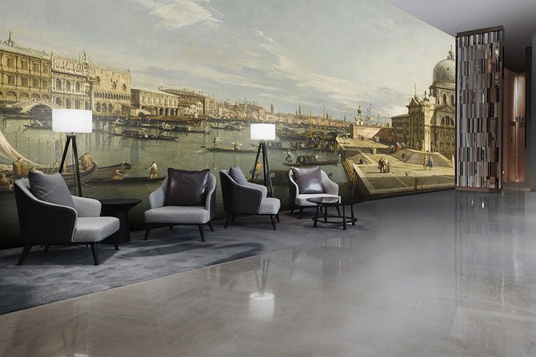 Salon moderne avec quatre fauteuils gris, des lampadaires et une grande fresque murale représentant une scène historique d'un canal vénitien.