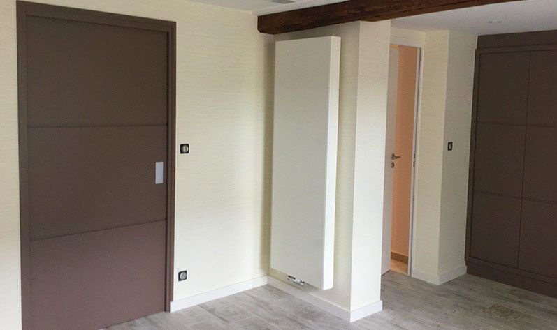 Intérieur d'une chambre moderne avec une porte marron foncé, un radiateur mural vertical blanc et une armoire encastrée marron foncé.