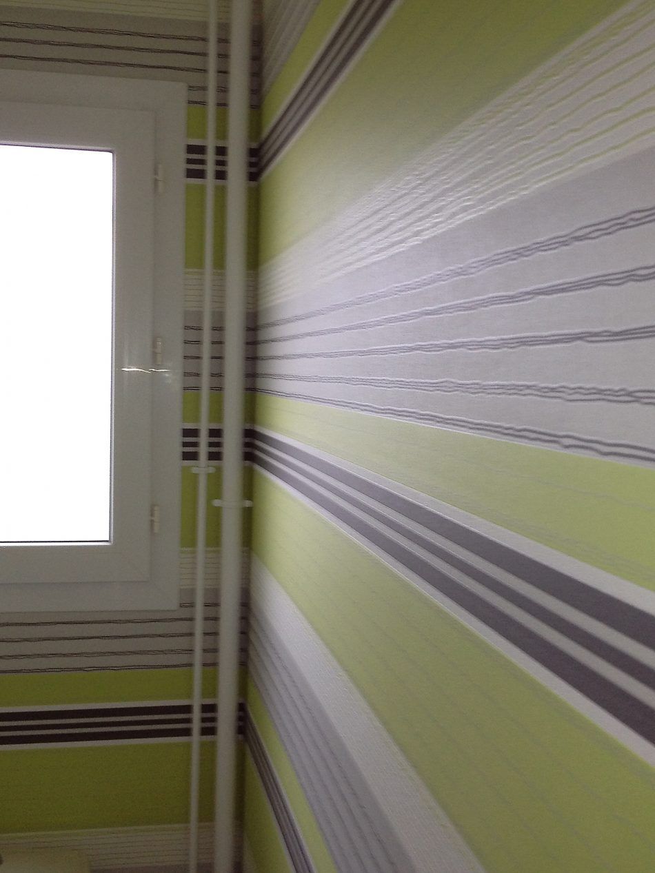 Gros plan sur un coin intérieur montrant des tuyaux verticaux blancs sur des murs recouverts de papier peint à rayures horizontales.