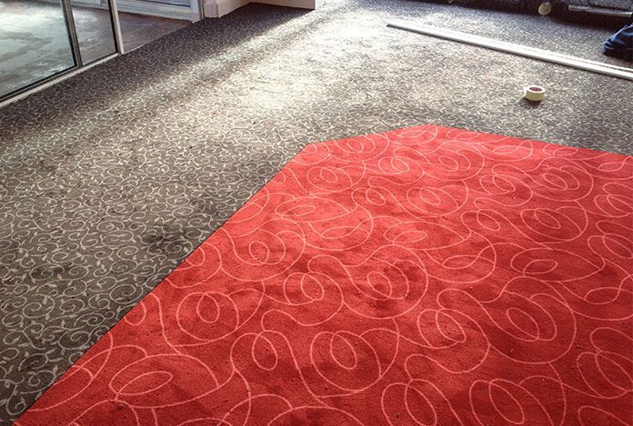 Un tapis rouge vif à motifs tourbillonnants blancs est posé sur le sol sombre et à motifs de la pièce.