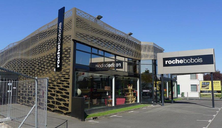 Un magasin de meubles Roche Bobois moderne, avec des murs métalliques à motifs en treillis et une grande enseigne de la marque en façade.