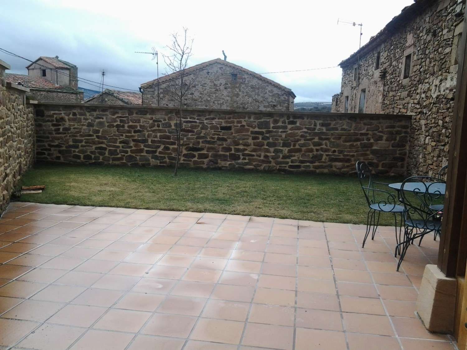 Un patio de piedra embaldosada conduce a un césped verde rodeado por un muro de piedra rústica .