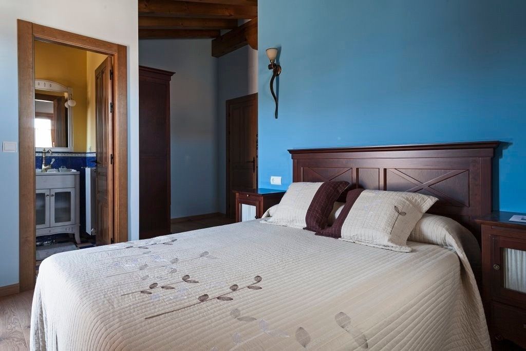 En una habitación, una cama con un edredón color crema se apoya contra una pared azul brillante.