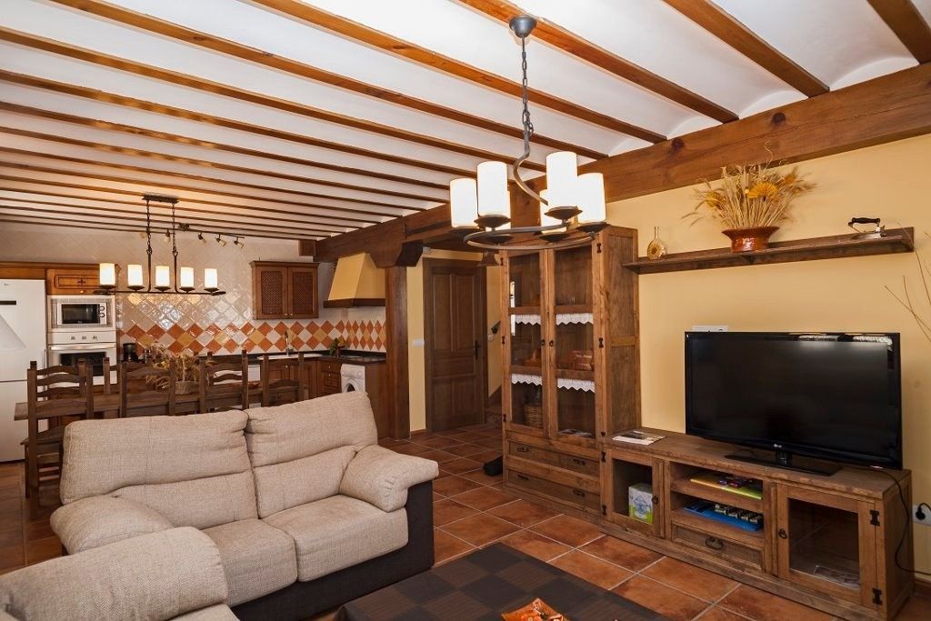 Una sala de estar rústica con vigas de madera a la vista en el techo, un sofá color crema, suelo de baldosas.