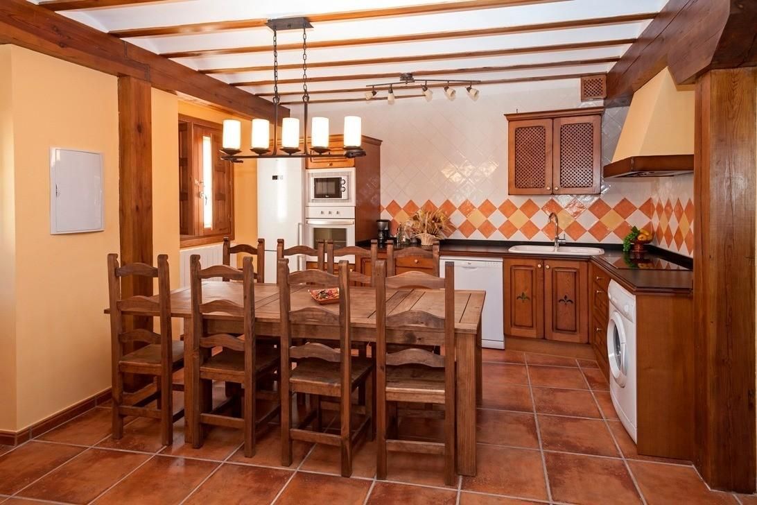 Cocina rústica con mesa y sillas de madera, suelo de baldosas de terracota y vigas de madera en el techo.