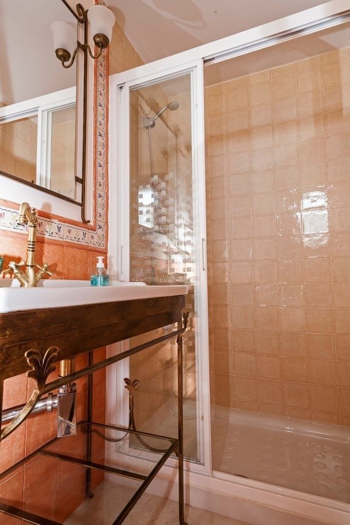 Un baño con lavabo de pedestal, grifo dorado, espejo de pared y ducha con mampara de cristal .