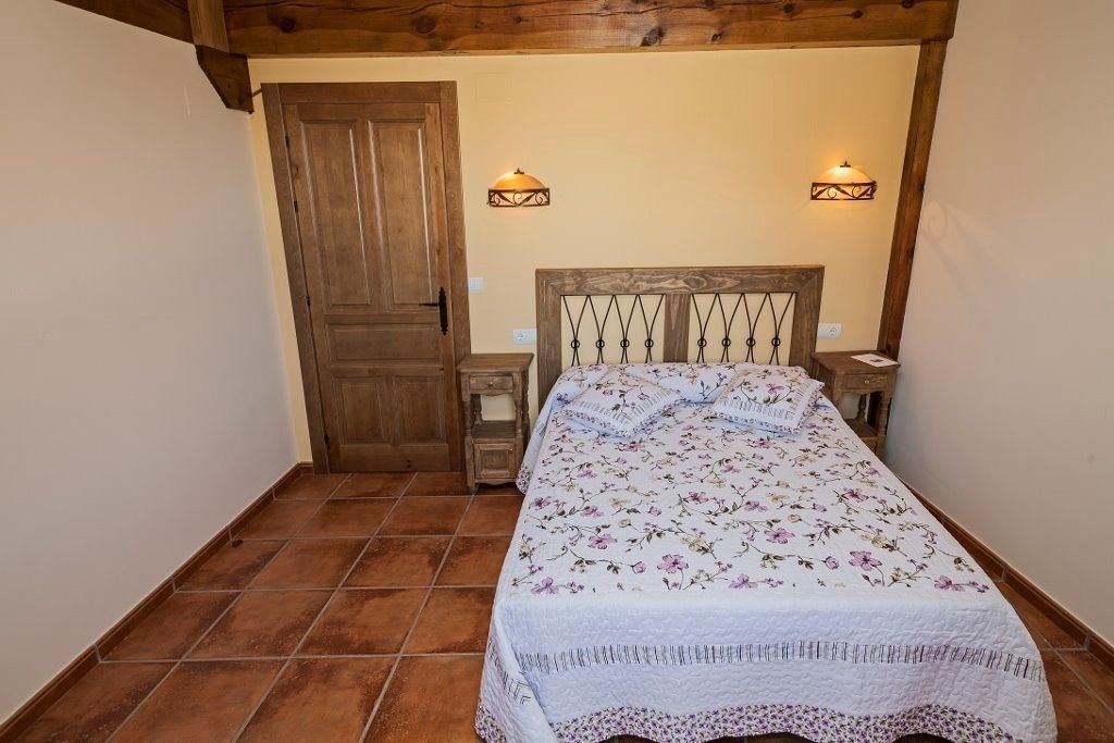 Un dormitorio con una colcha floral, cabecero de madera, mesitas de noche a juego y suelo de baldosas .